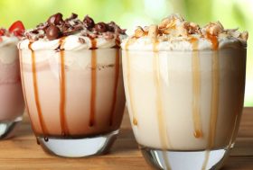 Tres vasos con cocteles y toppings de fresa, chocolate y caramelo.