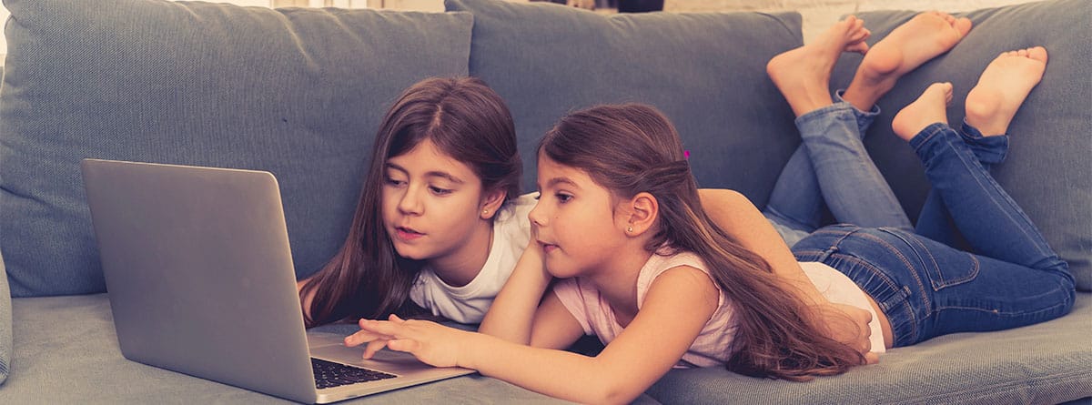 Dos niñas miran algo en una tablet que comparten tumbadas en un sofá