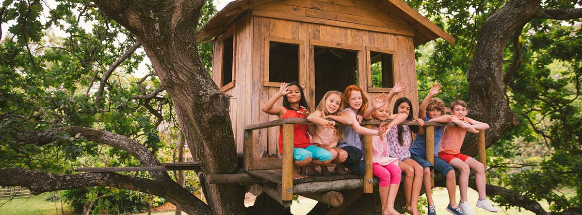 grupo de niños sentados en la entrada de una casita de madera en un árbol