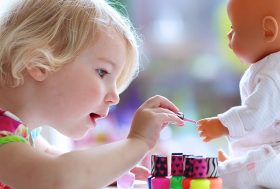 Niña pequeña pintando a un nenuco las uñas con pintauñas