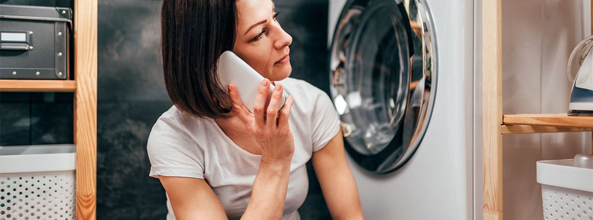 Mujer con cara de preocupada, hablando por el móvil, con una lavadora de fondo