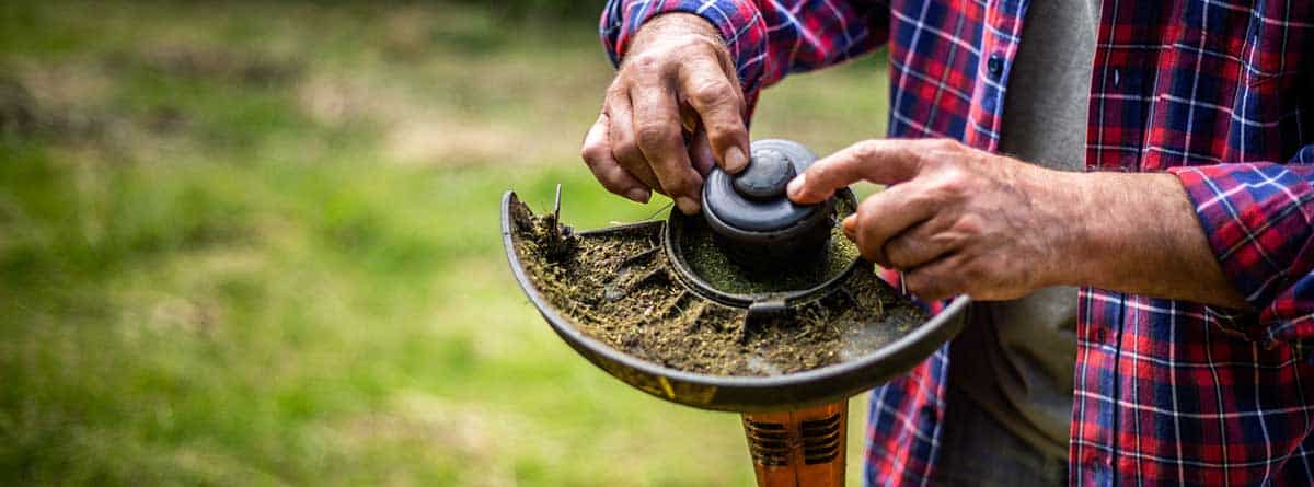 Mano masculina cambiando el hilo de una desbrozadora