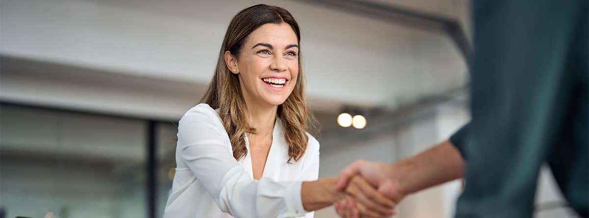 Una mujer sonriente da la mano a otra como firmando un acuerdo