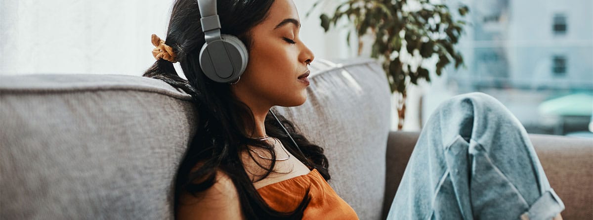 Mujer con auriculares en las orejas sentada en un sofá